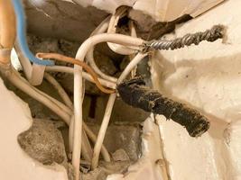 viejos cables retorcidos enredados en telarañas y polvo en un agujero en una pared en un sitio de construcción. electricista industrial muy pobre foto