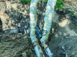 tendido de comunicaciones subterráneas para edificios residenciales. tuberías de fontanería en negro con una válvula envuelta en material blanco para regular el flujo de agua foto