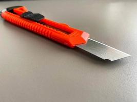 Red sharp office stationery knife with a paper cutting blade on a desktop office desk. Business work photo