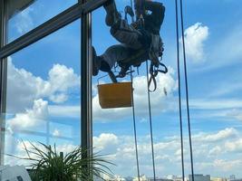 A male window washer worker, industrial climber hangs on a tall building, skyscraper and washes large glass windows for cleanliness high above a large city in an office business building photo