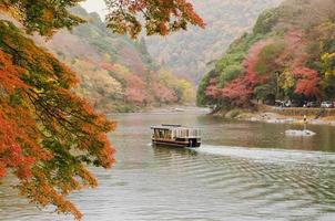 barco navegando a lo largo del río katsura en arashiyama, ciudad de kyoto en japón con coloridas hojas de arce de la temporada de otoño. foto