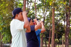 Three Asian boys use binoculars to look at birds in a community forest. own. The concept of learning from learning sources outside the school. Focus on the first child. photo