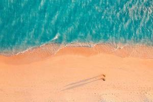 Aerial view of amazing beach with couple walking in sunset light close to turquoise sea. Top view of summer beach landscape, romantic inspirational couple vacation, romantic holiday. Freedom travel photo