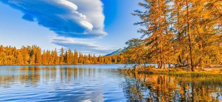Colorful autumn sunrise clouds sky over lake. Panoramic nature landscape, peaceful dream water surface, sunset autumnal background. Forest lake, mountains around. Peaceful amazing nature panorama
