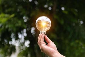 Hand holding light bulb on grass with solar energy and green background. photo