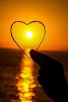 Hand holding heart shaped glass with sunset background photo