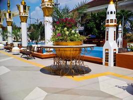 Large flower pot with golden iron carvings, Arabic style architecture, colorful flowers growing, bright blue clouds. photo