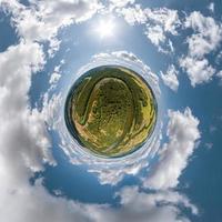 green tiny planet in blue overcast sky with beautiful clouds with transformation of spherical panorama 360 degrees. Spherical abstract aerial view. Curvature of space. photo