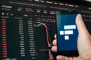 Man holding phone with FTX logo. Global fall of cryptocurrency graph - FTT token fell down on the chart crypto exchanges on app screen. FTX exchange bankruptcy and the collapse depreciation of token. photo