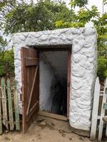 puerta abierta histórica bodega de raíces excavada bajo tierra en el campo cerca de los árboles. foto