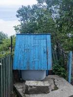 Ancient artesian well and wooden roof with hanging wood bucket in the village among the trees. photo