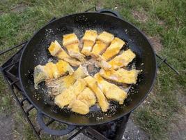 lucio asado en una sartén al fuego. pequeños trozos de pescado crujientes se fríen en aceite. el concepto de cocinar alimentos en la naturaleza. poca profundidad de campo. foto