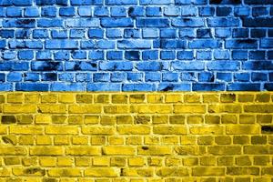 National flag of Ukraine painted on a brick wall. Banner on old brick wall background in cracks blue and yellow colors. The concept of relations between countries - no war between Ukraine and Russia. photo