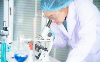 Asian woman scientist, researcher, technician, or student conducted research or experiment by using microscope which is scientific equipment in medical, chemistry or  biology laboratory photo