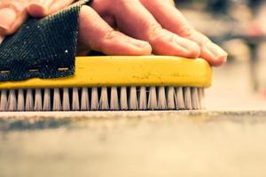 Hand hold brush and brushing wax on snowboard close up. Snowboard preparation in ski repair shop photo