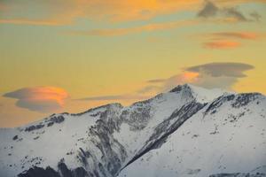 Panoramic view of beautiful winter wonderland mountain scenery with beautiful cloud formations and orange sunset background in caucasus. Majestic evening light at sunset photo