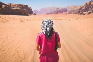 vista posterior del puesto de turista femenino ver señalar con el dedo el paisaje desértico de wadi rum en la famosa reserva natural del desierto de jordania en oriente medio. explorar jordan banner foto