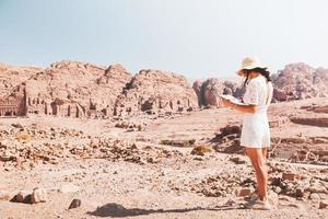 turista caucásica de moda, lee el mapa, planea explorar los lugares de interés de la antigua y fabulosa ciudad de petra en jordania. fotos coloridas. concepto de ocio, vacaciones y viajes.