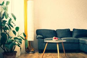 Cozy apartment living room with sofa and yellow pillows and stylish table with book by flower and window with blue light outside in winter. Early evening book read. Copy paste wall photo