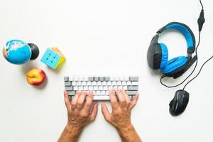 concepto de espacio de trabajo de teclado de tipo adulto infantil de jugador superior, vista superior de un equipo de juego, ratón, teclado, auriculares, sobre fondo de mesa blanco con espacio de copia y manzana foto