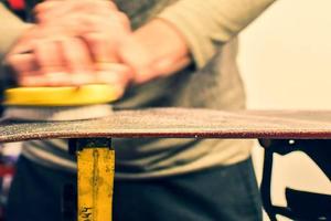 Hand hold brush and brushing wax on snowboard close up. Snowboard preparation in ski repair shop. Intentional blur photo