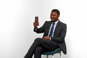 Smiling african american black man in business suit sitting on chair making video call via phone photo