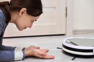 Friendly cheerful woman looking at robotic vacuum cleaner. photo