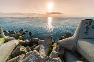 Beautiful sunset seascape. Breakwaters tetrapods ashore of pier. Cargo ships on the horizon. Travel dreams and motivation photo