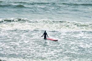 surfista masculino en traje de baño en el mar con tabla de surf roja foto