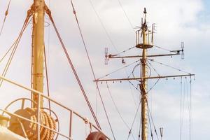 Ship mast of frigate, longboat or navy battleship. Metal mast pole. Ship awaits captain at docks. Lowered sails, blue sky on background. photo