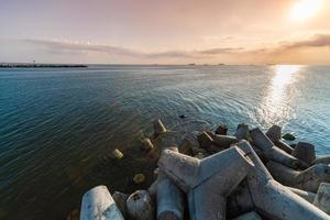 Beautiful sunset seascape. Breakwaters tetrapods ashore of pier. Cargo ships on the horizon. Travel dreams and motivation photo