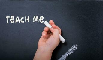 Hand with  white chalk and black board with teach me label