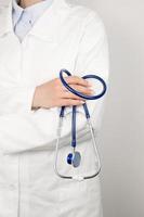 un médico con una bata médica blanca sostiene un estetoscopio en sus manos. concepto de salud. copie el fondo del espacio. pancarta vertical foto