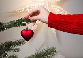 primer plano de manos femeninas sosteniendo adornos navideños en forma de corazón para decorar abetos. bandera de vacaciones de invierno foto