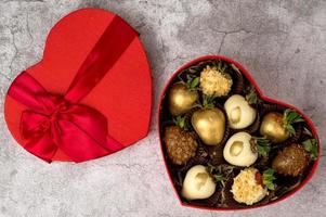 vista superior de la caja en forma de corazón con una variedad de fresas cubiertas de chocolate sobre un fondo gris. San Valentín, concepto del día de la madre foto