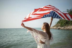 las mujeres jóvenes sostienen banderas americanas en la playa y el mar en sus vacaciones de verano y sonríen y disfrutan de sus vacaciones. foto