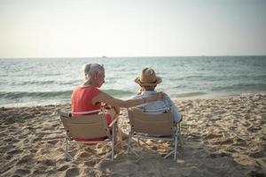 An elderly couple hugs their shoulders at the beach on their summer vacation and they smile and enjoy their vacation. photo