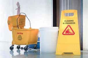 Close up yellow warning sign with message Cleaning in progress with cleaning trolley background photo