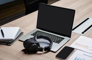 pantalla en blanco del portátil, auriculares y papeleo en la mesa foto