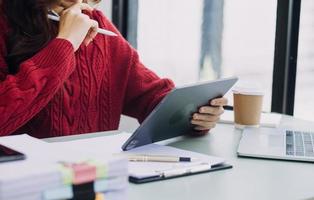 Young business woman sitting in office at table and using smartphone. On desk is laptop and tablet computer, on screen charts and graphs. Woman analyzing data. Student learning online. photo