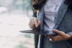 Young business woman sitting in office at table and using smartphone. On desk is laptop and tablet computer, on screen charts and graphs. Woman analyzing data. Student learning online. photo