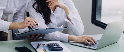 Young business woman sitting in office at table and using smartphone. On desk is laptop and tablet computer, on screen charts and graphs. Woman analyzing data. Student learning online. photo