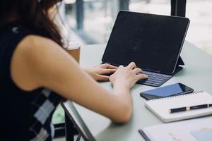 Young business woman sitting in office at table and using smartphone. On desk is laptop and tablet computer, on screen charts and graphs. Woman analyzing data. Student learning online. photo
