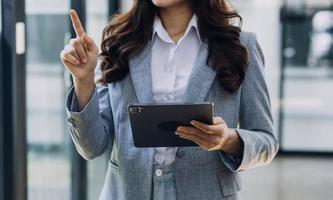 Young business woman sitting in office at table and using smartphone. On desk is laptop and tablet computer, on screen charts and graphs. Woman analyzing data. Student learning online. photo