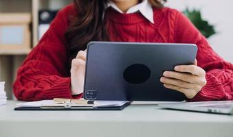 Young business woman sitting in office at table and using smartphone. On desk is laptop and tablet computer, on screen charts and graphs. Woman analyzing data. Student learning online. photo