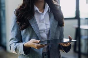 Young business woman sitting in office at table and using smartphone. On desk is laptop and tablet computer, on screen charts and graphs. Woman analyzing data. Student learning online. photo