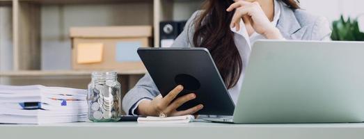 Young business woman sitting in office at table and using smartphone. On desk is laptop and tablet computer, on screen charts and graphs. Woman analyzing data. Student learning online. photo