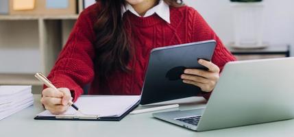 Young business woman sitting in office at table and using smartphone. On desk is laptop and tablet computer, on screen charts and graphs. Woman analyzing data. Student learning online. photo