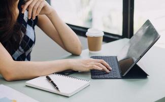Young business woman sitting in office at table and using smartphone. On desk is laptop and tablet computer, on screen charts and graphs. Woman analyzing data. Student learning online. photo