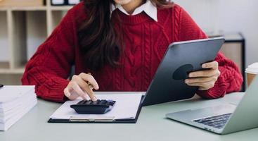 Young business woman sitting in office at table and using smartphone. On desk is laptop and tablet computer, on screen charts and graphs. Woman analyzing data. Student learning online. photo